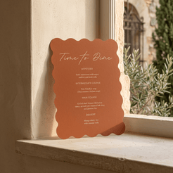 A terracotta-colored scalloped metal sign with white text reading 'Time to Dine' and a course list, displayed on a beige stone windowsill with a blurred outdoor garden background.