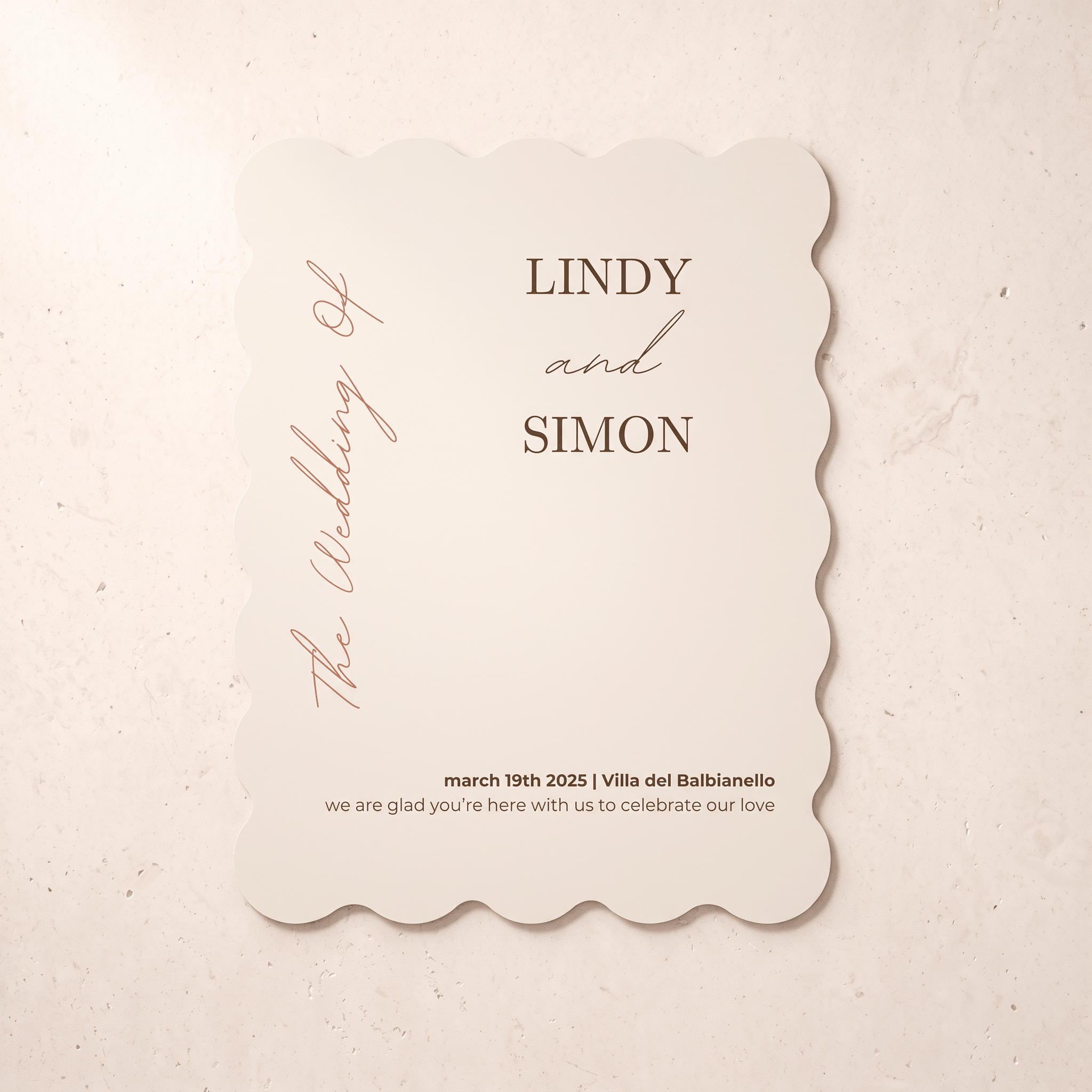 A scalloped-edge wedding invitation card with a warm cream background and brown text, reading 'LINDY and SIMON' and 'The Wedding of' in elegant script, placed on a light beige textured surface.