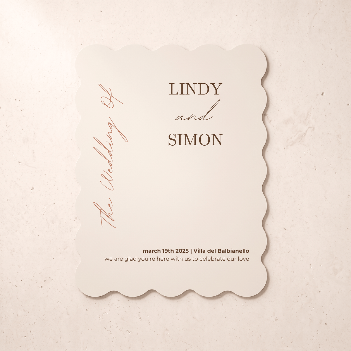 A scalloped-edge wedding invitation card with a warm cream background and brown text, reading 'LINDY and SIMON' and 'The Wedding of' in elegant script, placed on a light beige textured surface.
