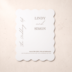 A scalloped-edge white wedding invitation card with elegant gray typography, displayed flat on a textured beige surface. The card features placeholder names 'LINDY and SIMON' and wedding details.