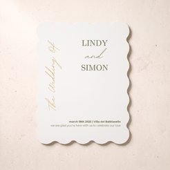 A scalloped-edge white wedding invitation card with elegant gold typography, displayed flat on a light beige textured background. The card features the names 'LINDY and SIMON' and wedding details for March 19th, 2025, in Villa del Balbianello.
