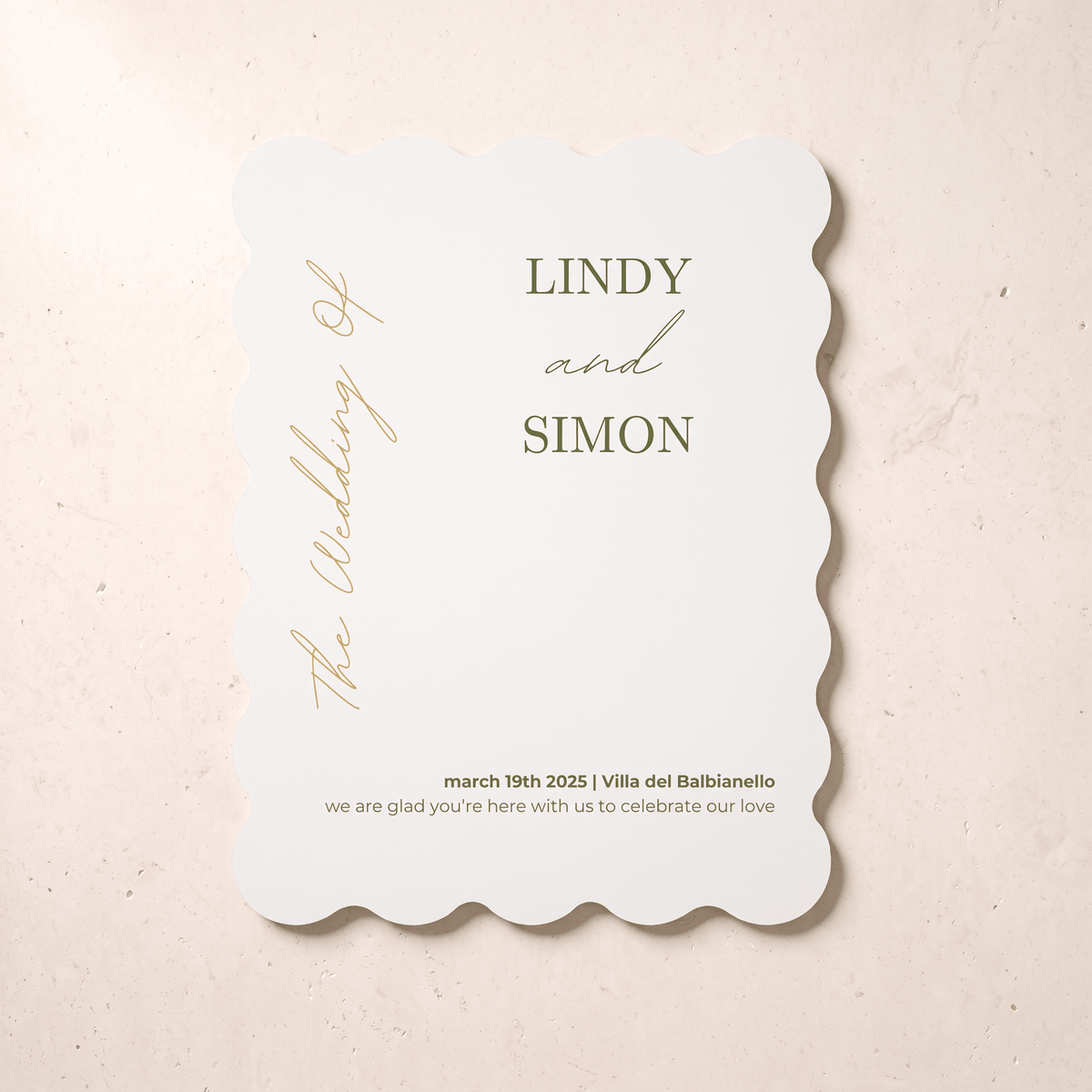A scalloped-edge white wedding invitation card with elegant gold typography, displayed flat on a light beige textured background. The card features the names 'LINDY and SIMON' and wedding details for March 19th, 2025, in Villa del Balbianello.