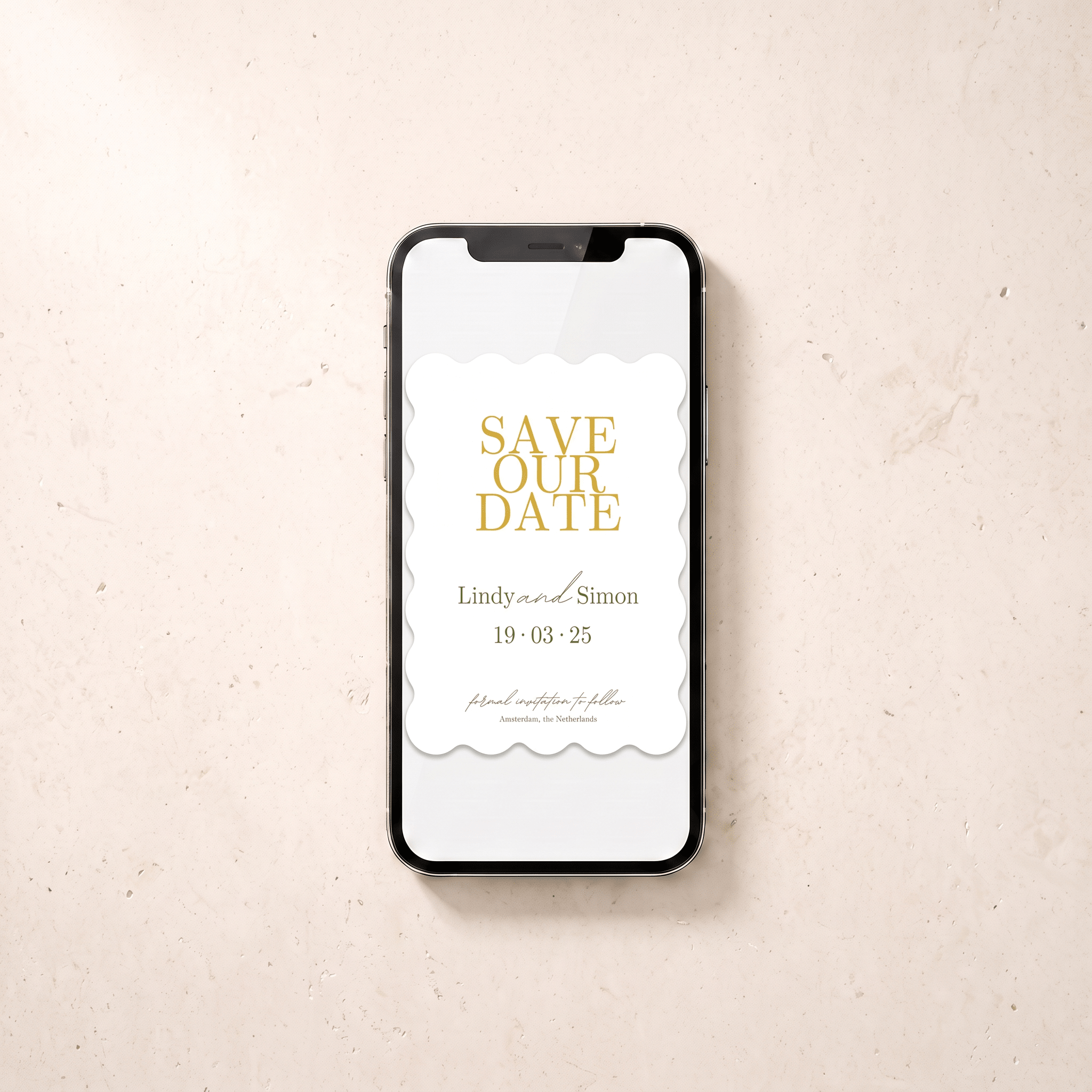 A smartphone lying on a light beige textured surface, displaying a white 'Save the Date' card design with gold typography and scalloped white paper-like borders.