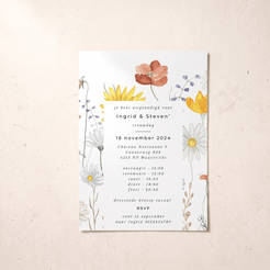 A vertical wedding invitation card with a white background and delicate watercolor floral illustrations in yellow, orange, blue, and white, placed on a textured beige surface.