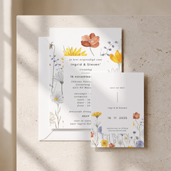 A floral wedding invitation suite styled on a textured beige stone surface with soft diagonal shadows. The set includes a main invitation card, a separate RSVP card, and an envelope, all decorated with delicate watercolor-style flowers in yellow, orange, blue, and purple tones.