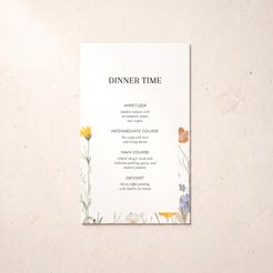 A vertical wedding program or dinner menu card with elegant black typography and delicate watercolor floral illustrations in yellow, orange, blue, and purple, displayed flat on a textured beige surface.