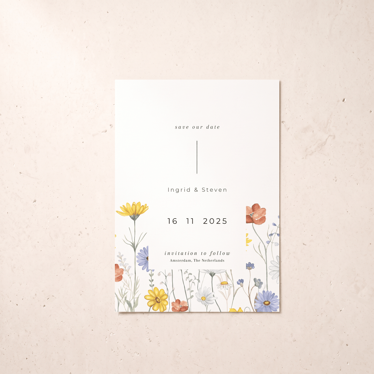 A vertical wedding save-the-date card with a white background and delicate watercolor floral illustrations along the bottom, displayed on a textured beige surface.