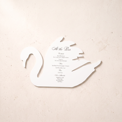 A white swan-shaped paper menu card with elegant black script and serif text reading 'At the Bar' and a list of course titles, placed on a light beige textured surface.
