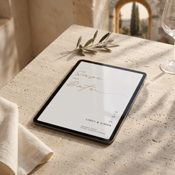 A tablet lying on a light stone tabletop in a sunlit real environment, displaying a minimalist 'Save the Date' card design with elegant script and small event text.