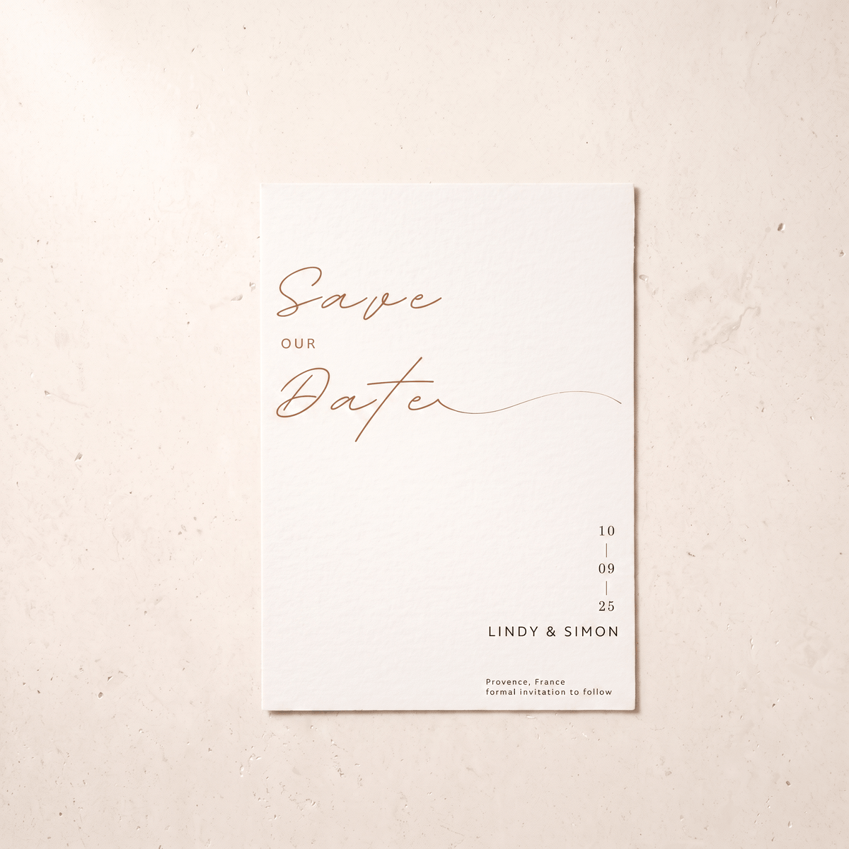 A minimalist 'Save Our Date' wedding card with elegant rose gold script and black text on a clean white card, displayed flat on a textured beige surface.