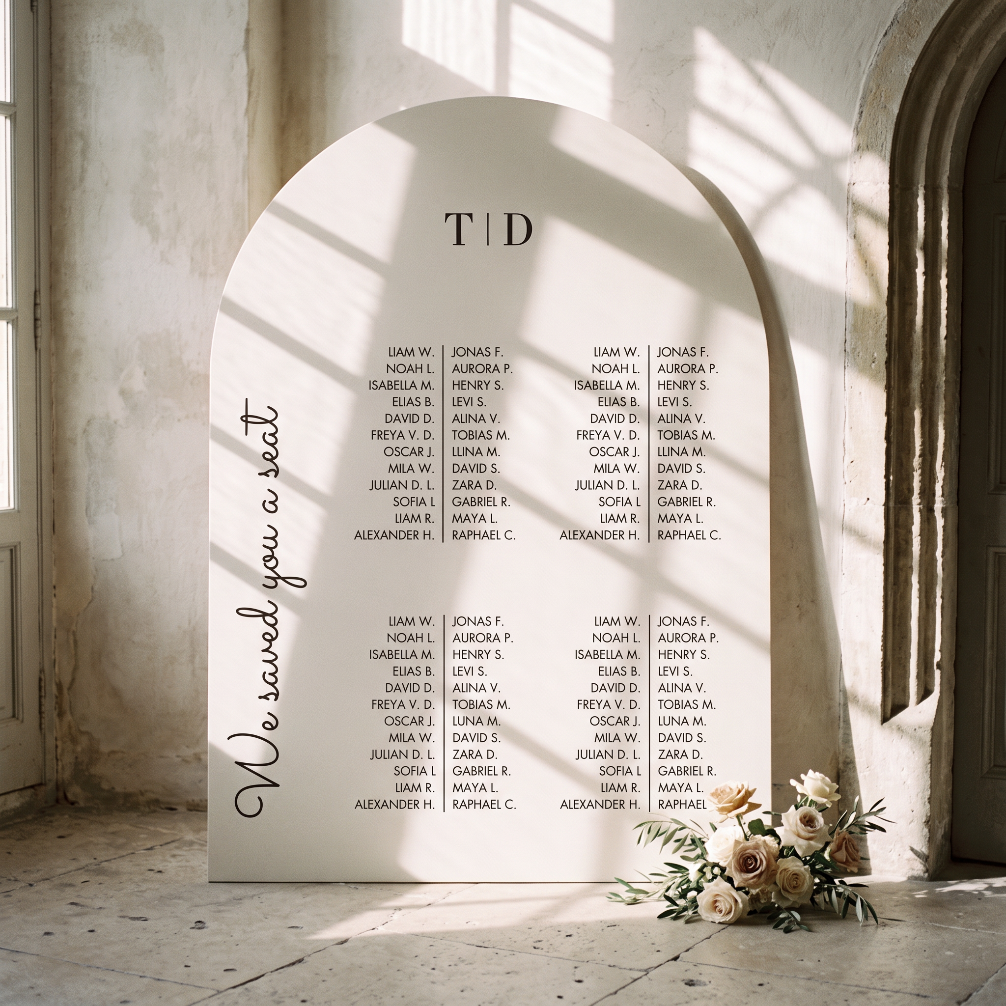 A large arched white wedding seating sign displayed in a sunlit stone interior. The sign reads 'We saved you a seat' and lists names under the heading 'TID'.